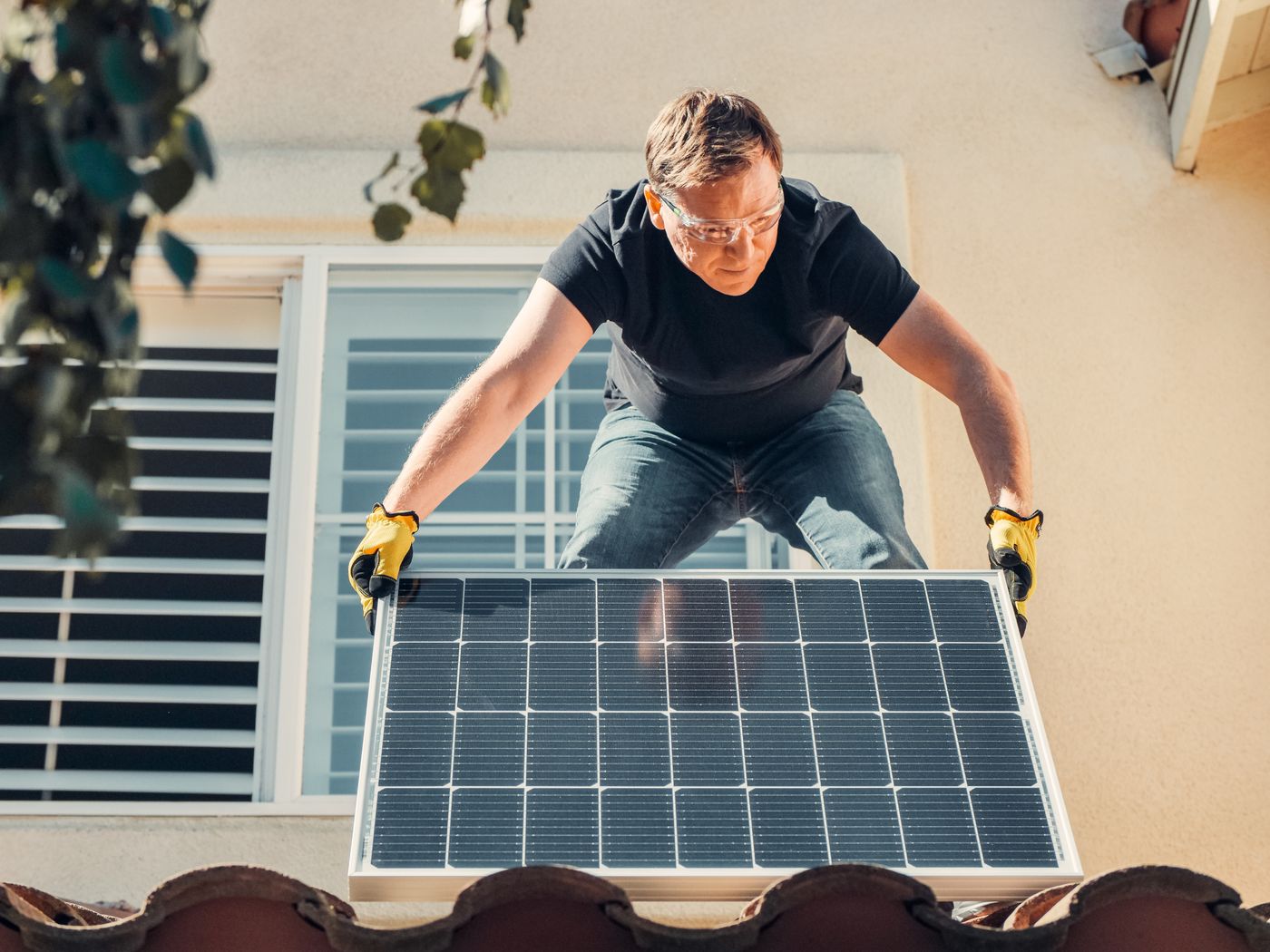 Illustrative photo: a solar installer carrying a panel on a house roof